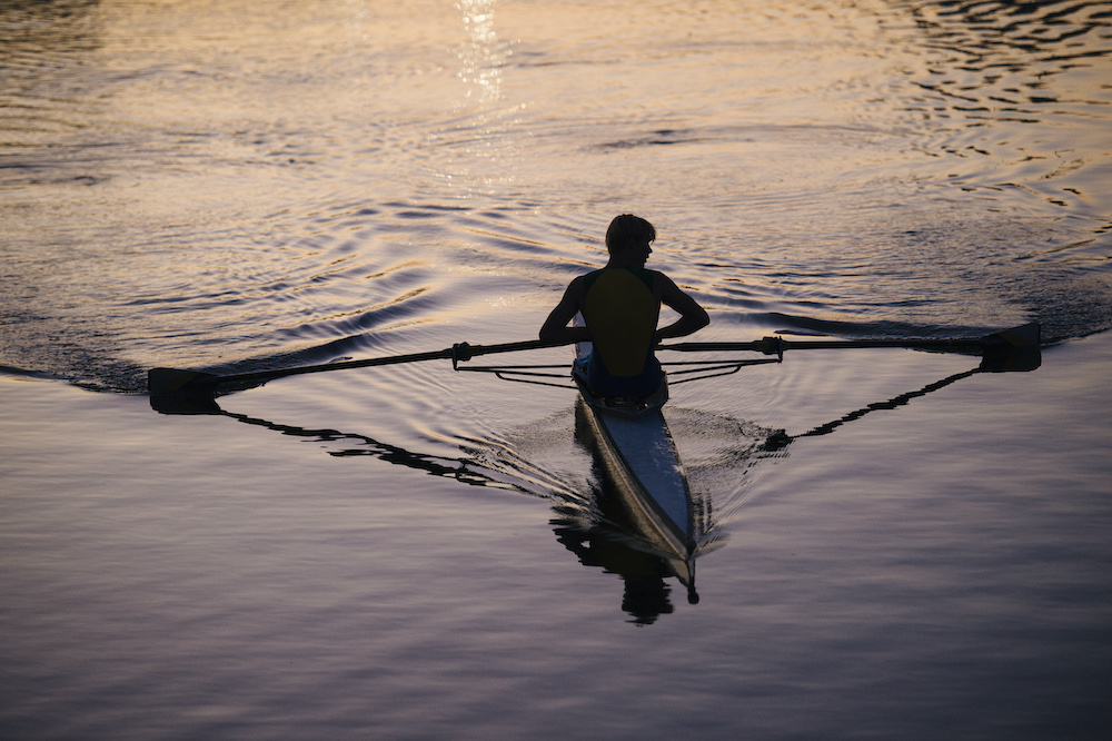 Young man rowing on river at sunset